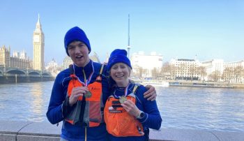Two paddlers stand with somewhat shocked, confused, and happy expressions in front of Big Ben holding their DW finishers medals