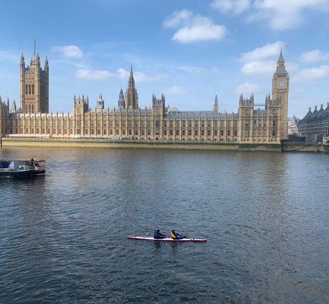 A crew in a two-person skinny kayak (K2) finishes in front of Big Ben and the Houses of Parliament looking small against the wide river