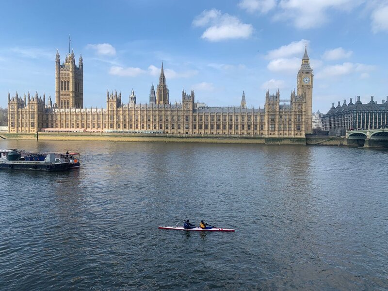 A crew in a two-person skinny kayak (K2) finishes in front of Big Ben and the Houses of Parliament looking small against the wide river